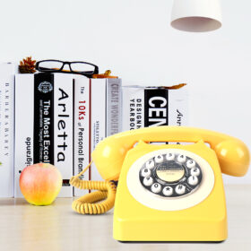  Yellow rotary telephone on a wooden desk with books and apple