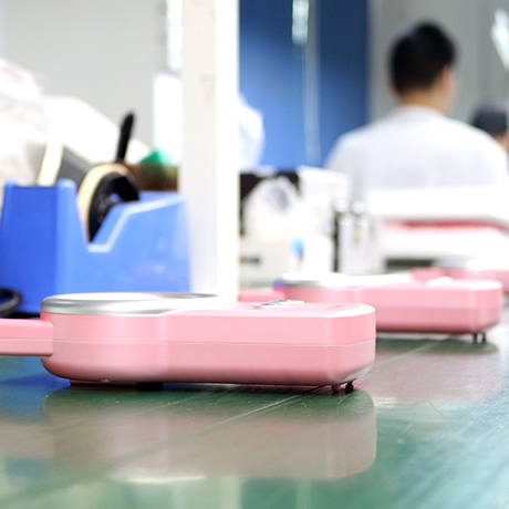 Download section image in 460x461 pixels showing a pink communication device placed on a production bench in a lab environment.